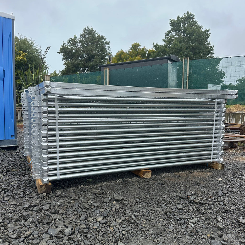 Stack of flat-packed galvanised yard panels on a gravel yard, ready for freight.